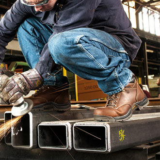 A man wearing brown work boots while using a power tool.