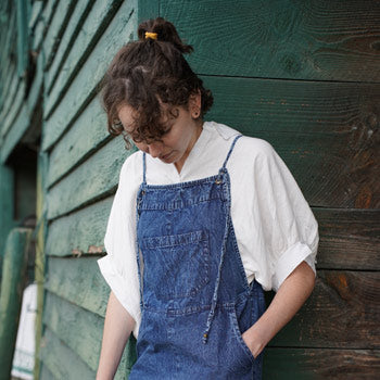 A person wearing blue overalls, looking down at their shoes.